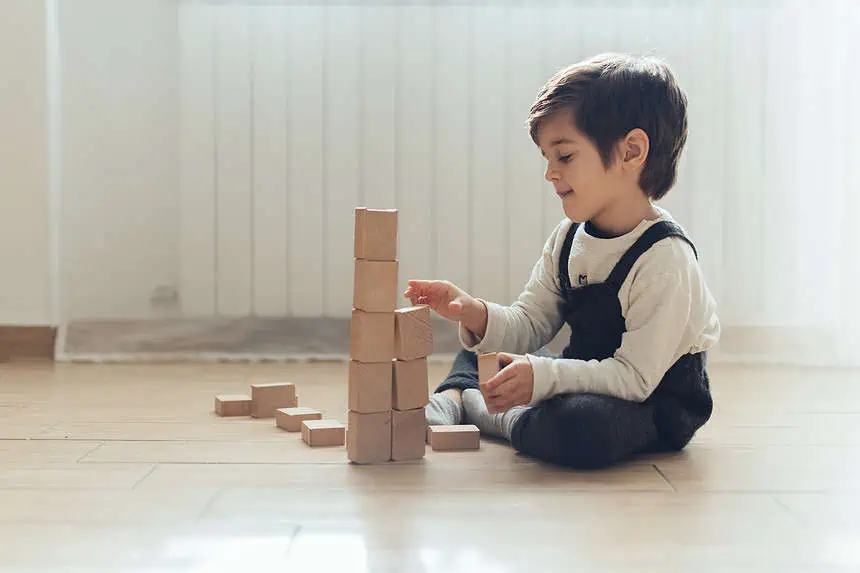Young boy stacking wooden blocks on the floor indoors.