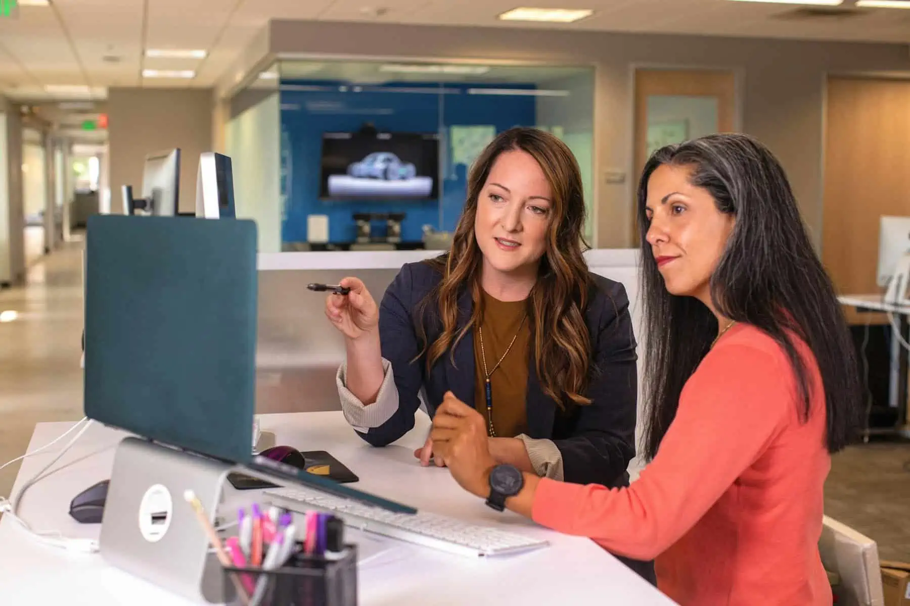 Women collaborating at work, discussing a project on a desktop computer in an office setting.