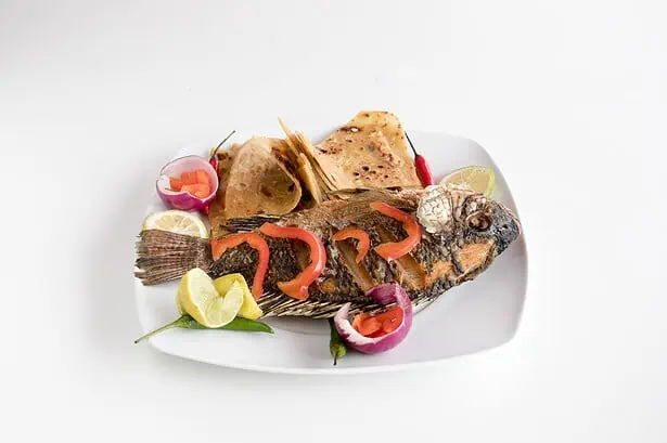 Delicious grilled fish served with lemon slices and fresh vegetables on a white plate.