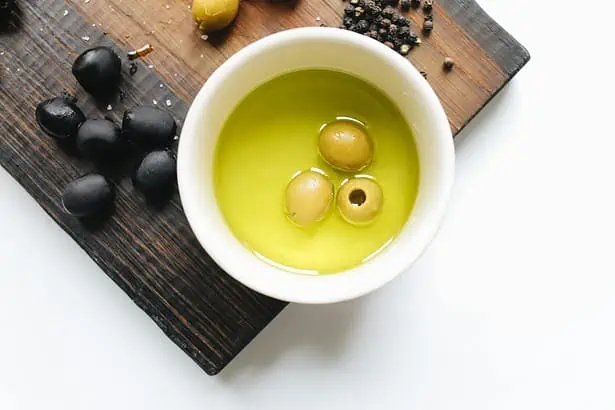 Bowl of fresh olive oil with green olives on a wooden board.