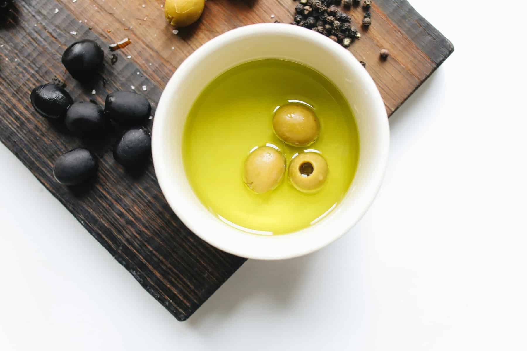 Home Icy 44 Bowl of fresh olive oil with green olives on a wooden board.