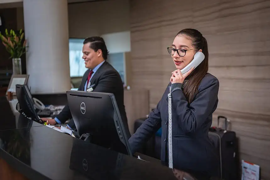 Reception staff assisting guest with phone call at hotel front desk.