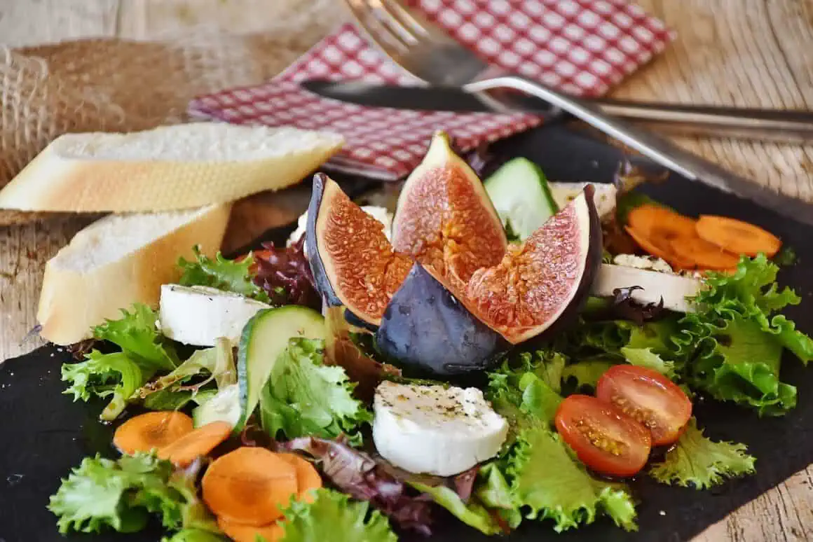 Colorful fresh fig and vegetable salad with cheese on a black plate.