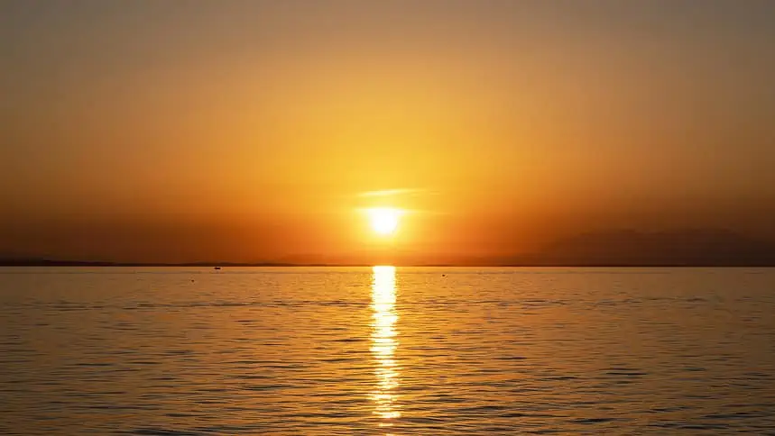 Sunset over the ocean with vibrant orange and yellow hues reflecting on the water surface.