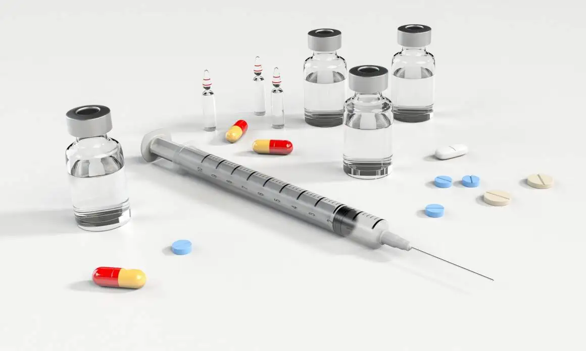 Vaccine vials, syringes, and pills arranged on a white background for medical treatment.