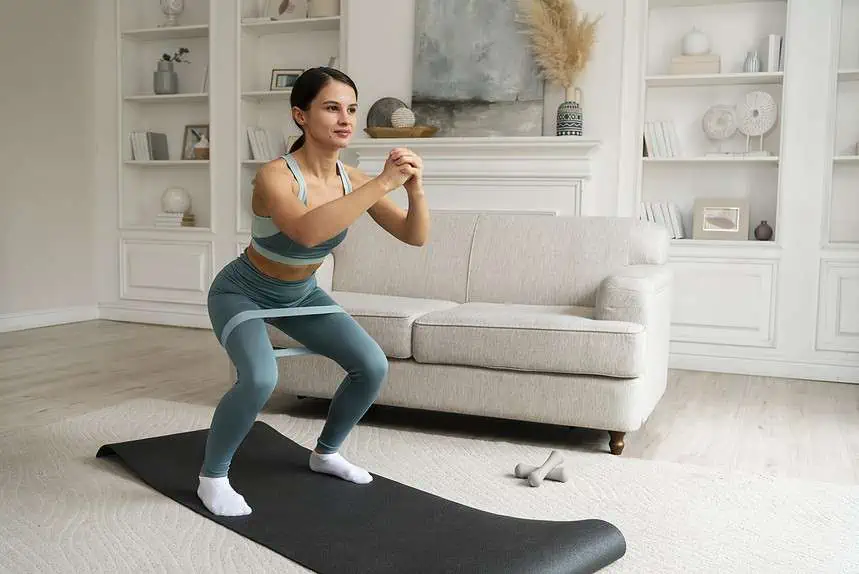 5 Tips for Setting Fitness Goals This Summer 1 Woman exercising at home with squat on yoga mat in living room.