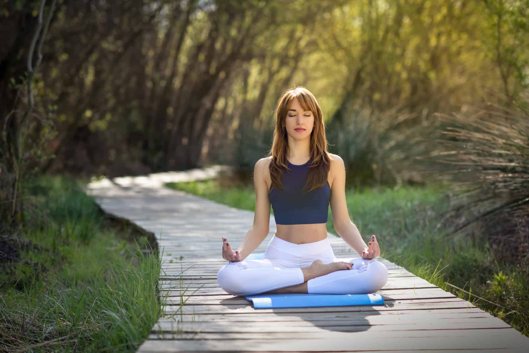 Woman meditating in a peaceful outdoor setting on a wooden pathway.