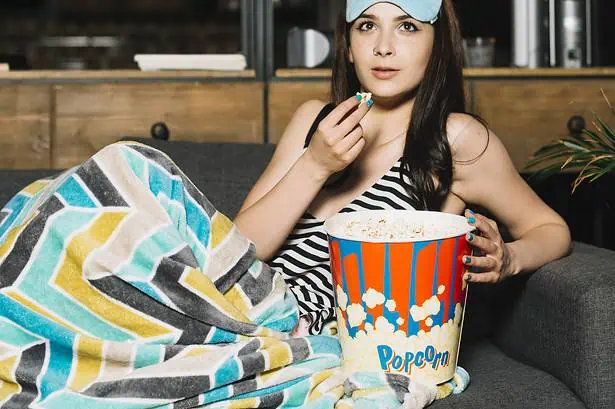 Woman watching movie with popcorn and sleep mask at home.