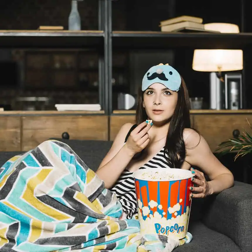 Woman watching movie with popcorn and sleep mask at home.