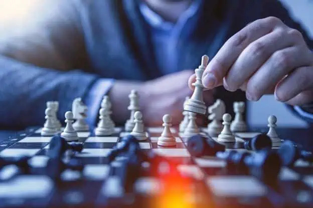 A person making a strategic move in a chess game, focusing on planning and tactics.