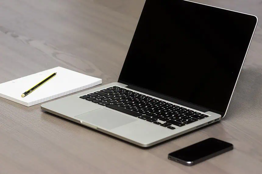 Laptop with black keyboard and blank screen, alongside a notebook, pen, and smartphone on a wooden d.