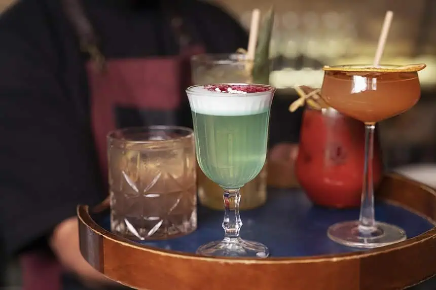Here is How You Can make Your Own Craft Cocktails in Your Home! 1 Vibrant cocktails with colorful layers and garnishes on a tray at a lively bar.