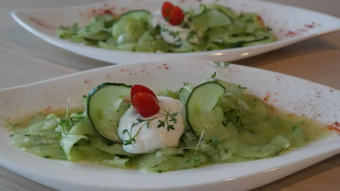 Fresh cucumber salad with cherry tomatoes and herbs on a white plate.