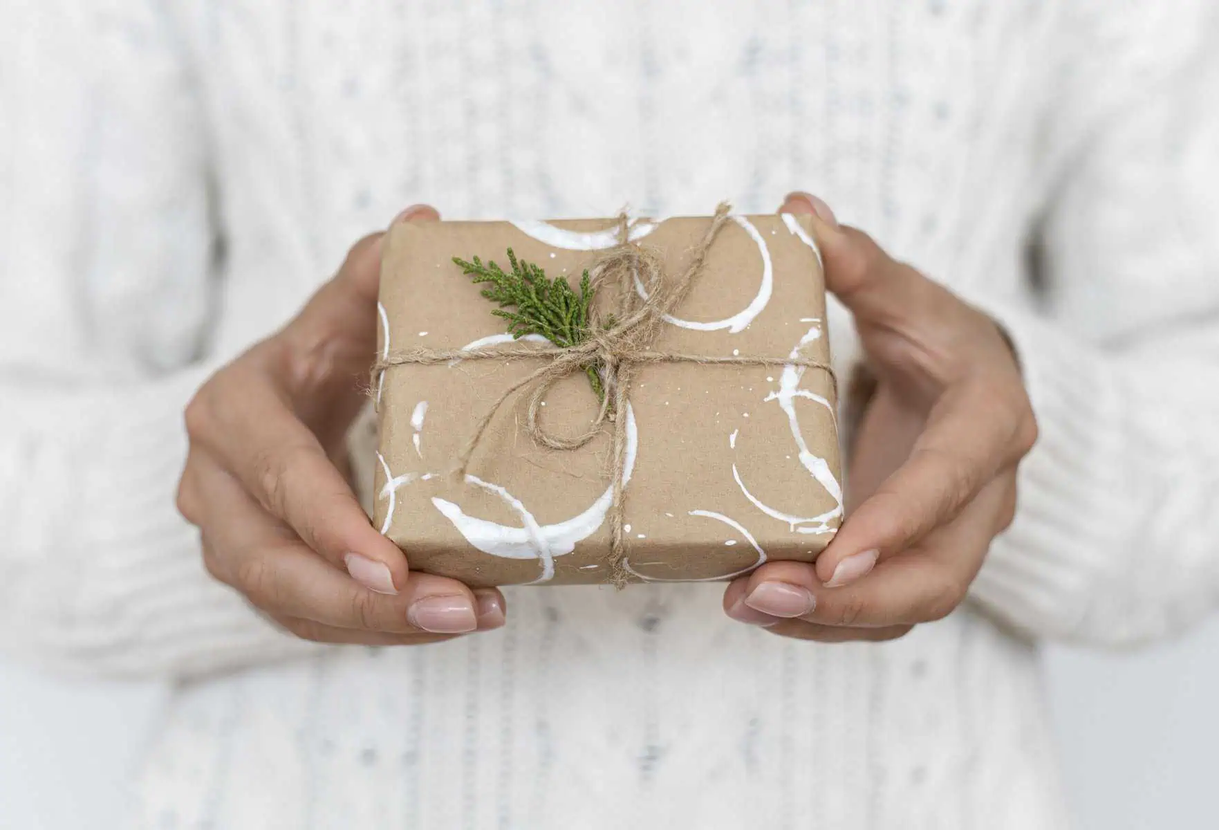 Hand holding a wrapped gift box with twine and greenery.