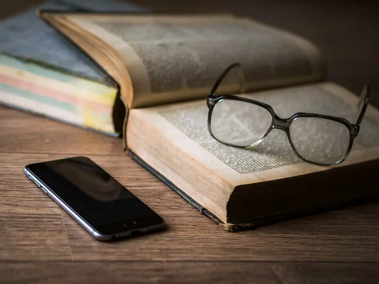 Open book with reading glasses and smartphone on wooden table, symbolizing study or research.