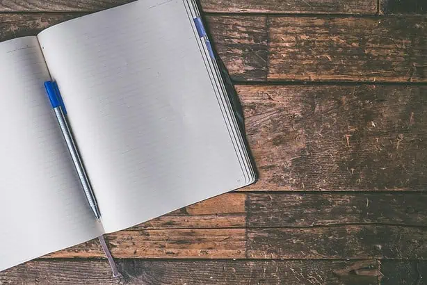 Open blank notebook with pen on rustic wooden table.