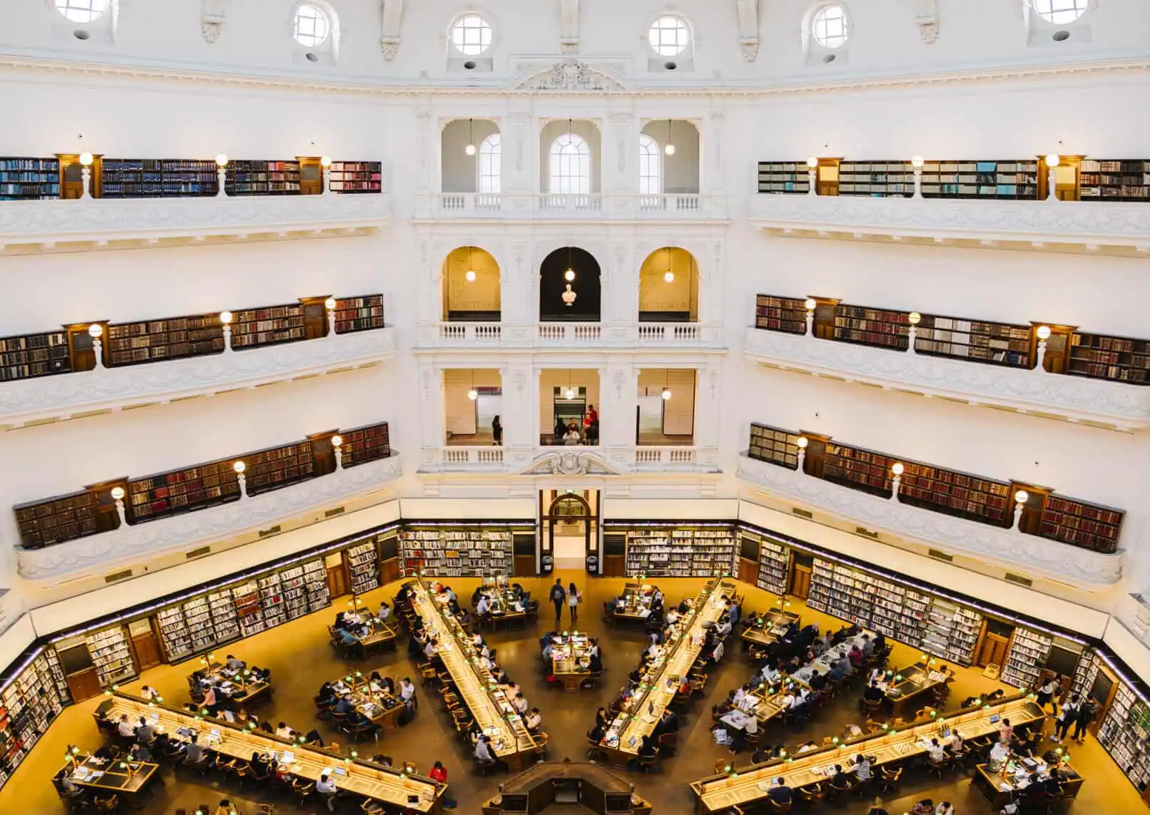 Library interior with tall bookshelves, reading tables, and natural light in a grand, multi-story se.