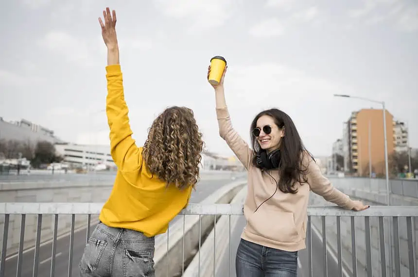 Two women celebrating with high-fives on a city bridge, showcasing friendship and outdoor fun.