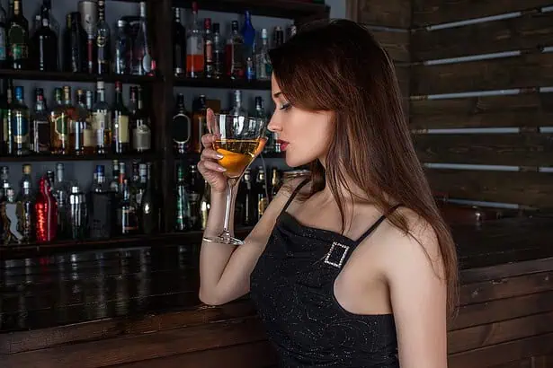 A woman enjoying a cocktail at a bar with shelves of liquor bottles in the background.