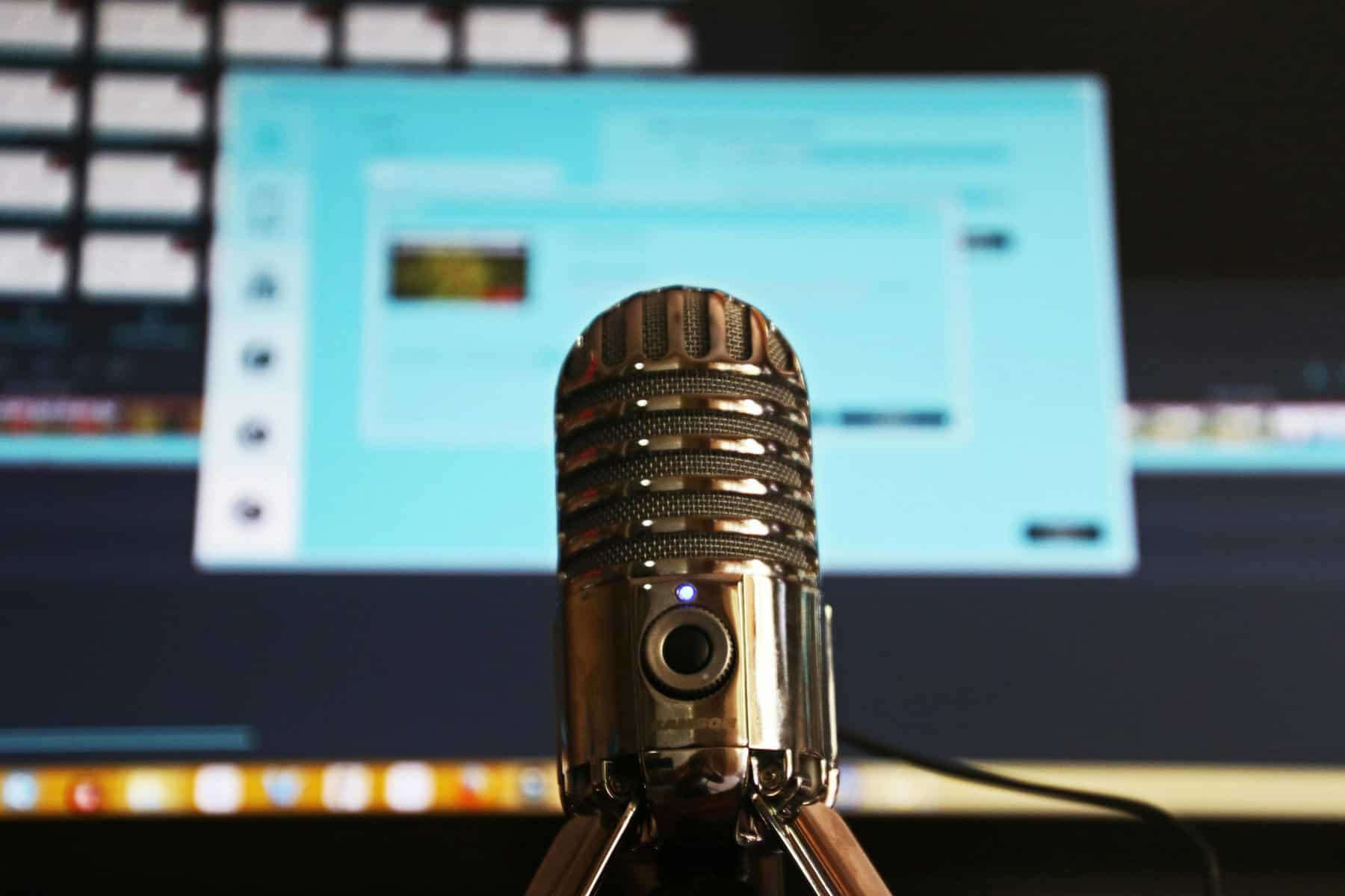 Microphone for recording or broadcasting with a blurred computer screen in the background.