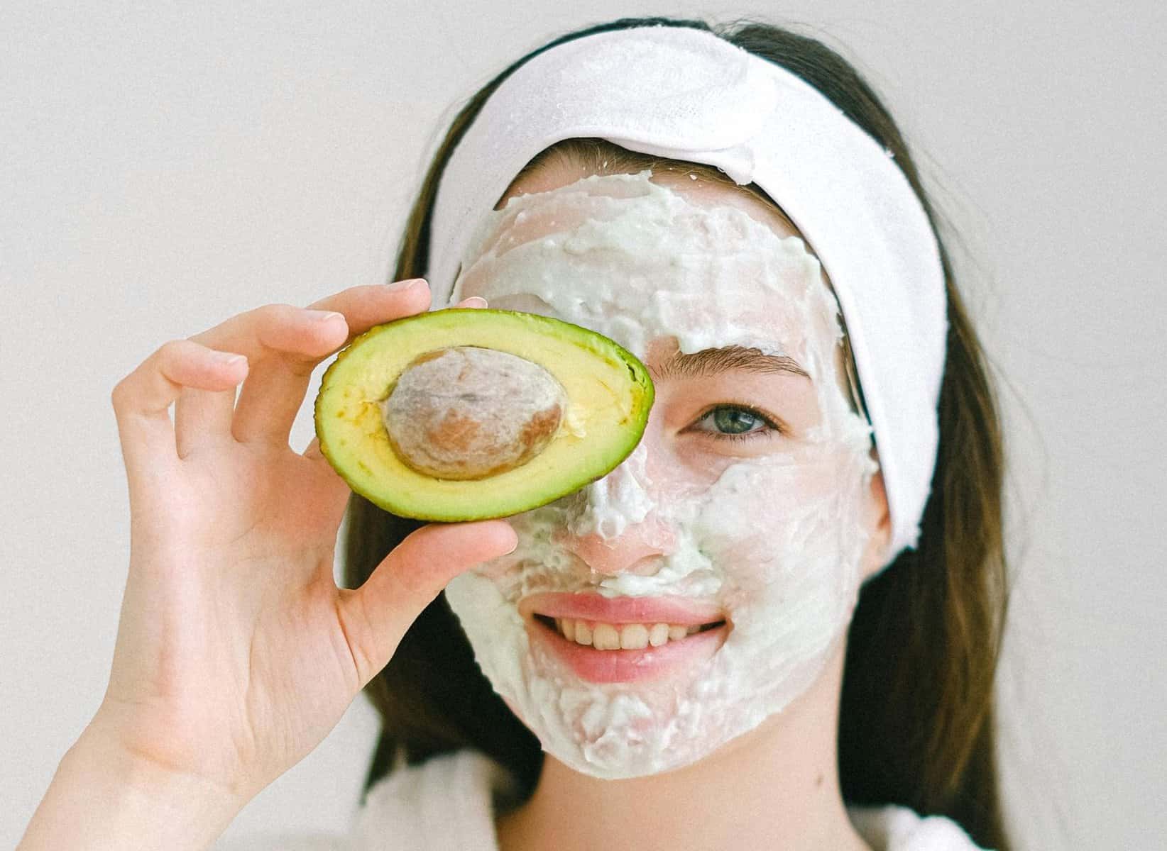 Home Icy 47 Woman with avocado face mask holding half avocado, skincare routine.