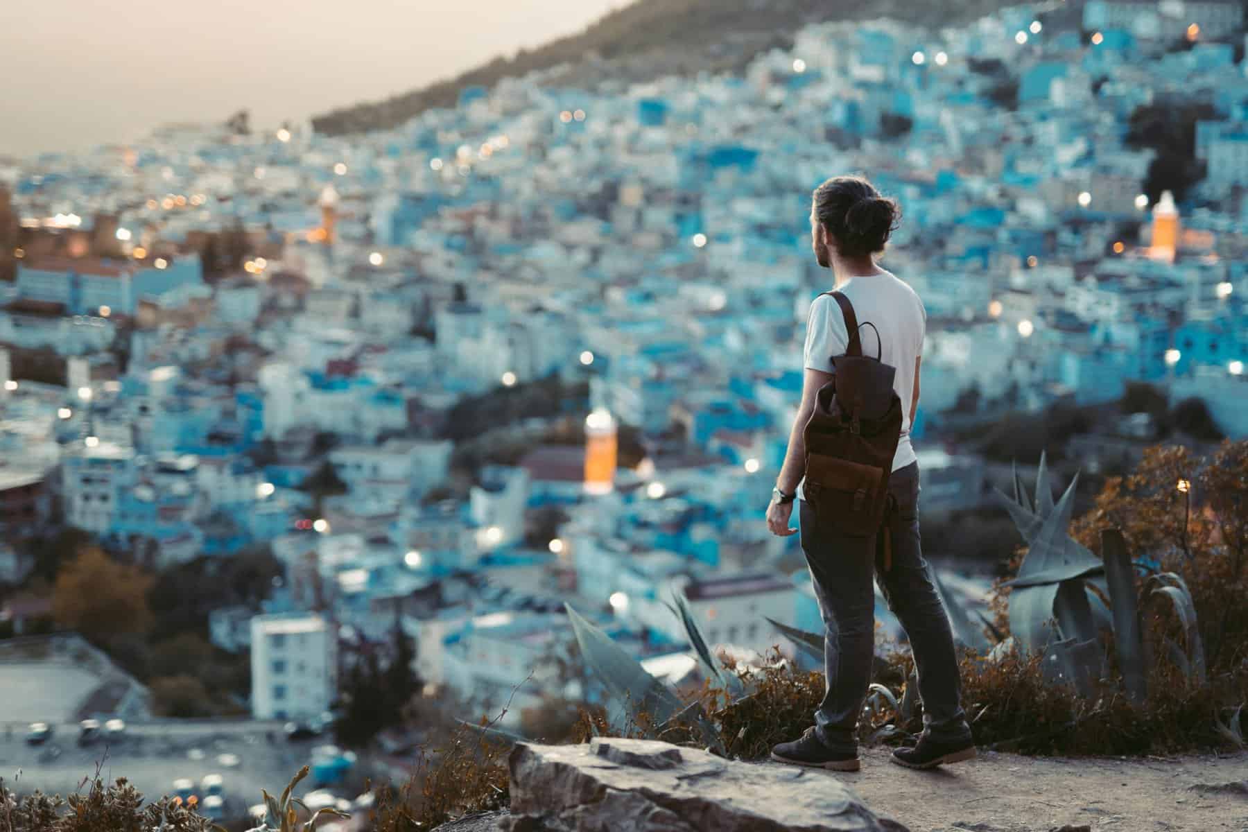 A woman standing on a hilltop, gazing at a vibrant cityscape illuminated at dusk, capturing a moment.