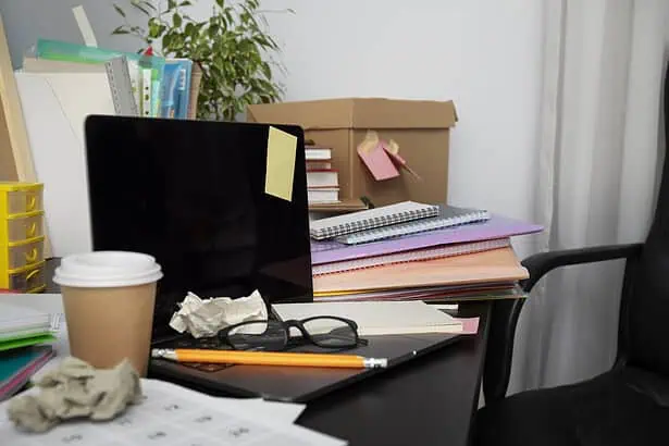 Work desk with a computer monitor, scattered papers, glasses, and a coffee cup, indicating a busy of.
