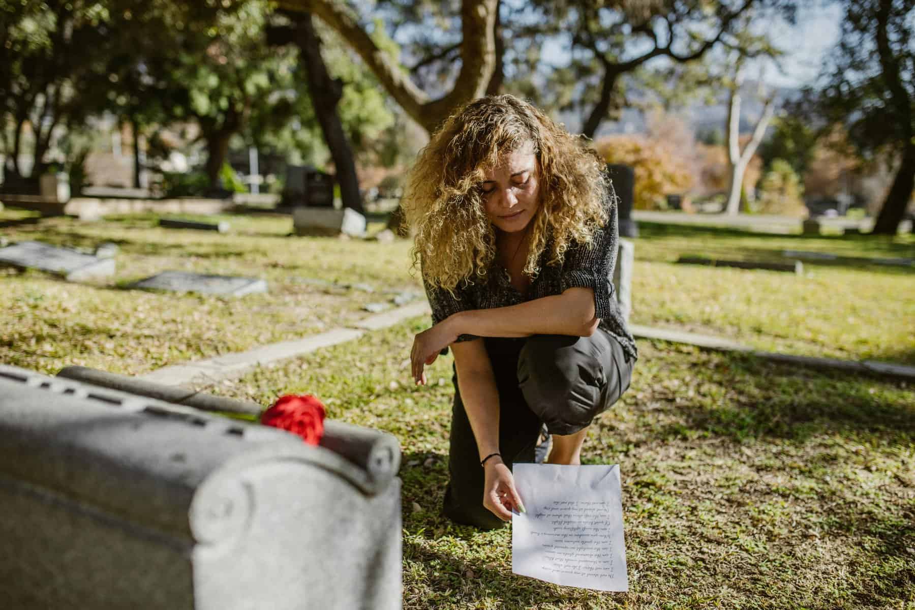 Home Icy 47 Memorial tribute by a woman placing a paper at a cemetery grave site.
