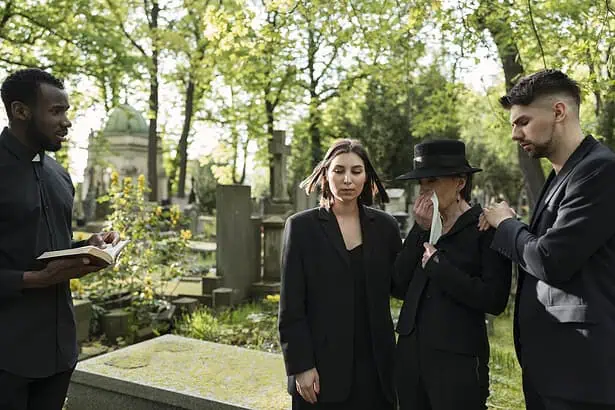 Group of people mourning at a cemetery during a funeral service.