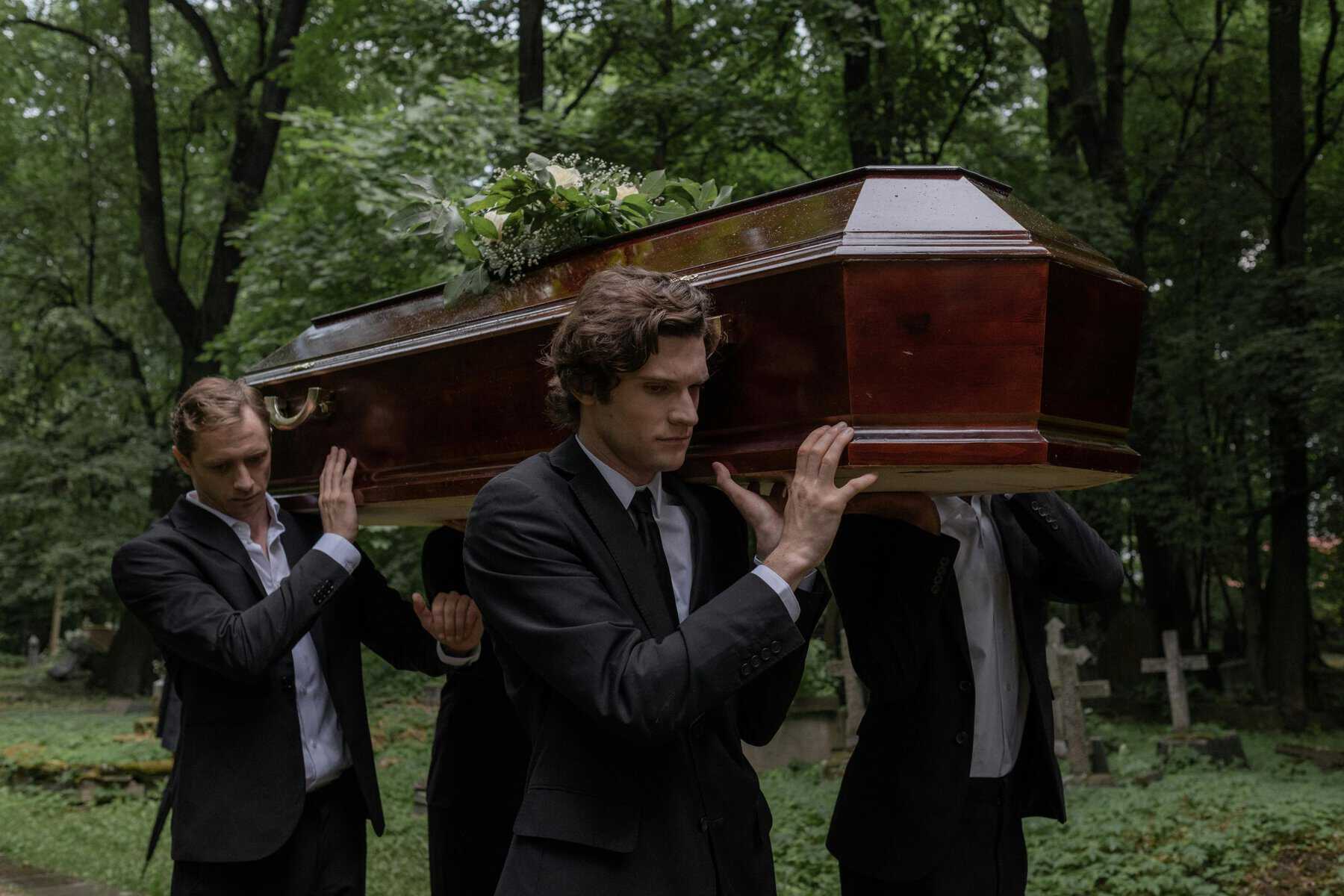 Coffin being carried by pallbearers during a funeral procession in a lush green forest.