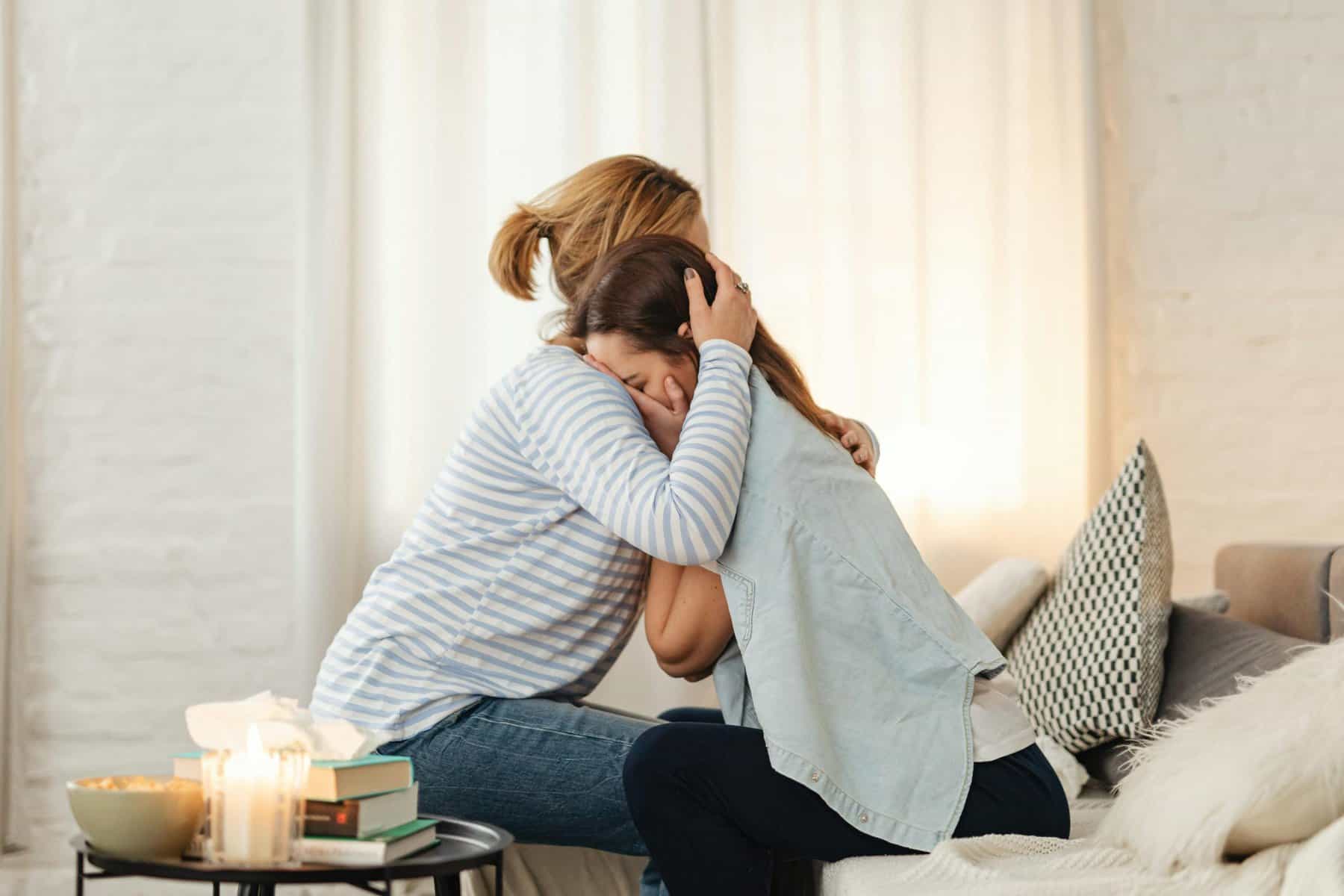 Woman comforting friend with a hug in a cozy living room setting.