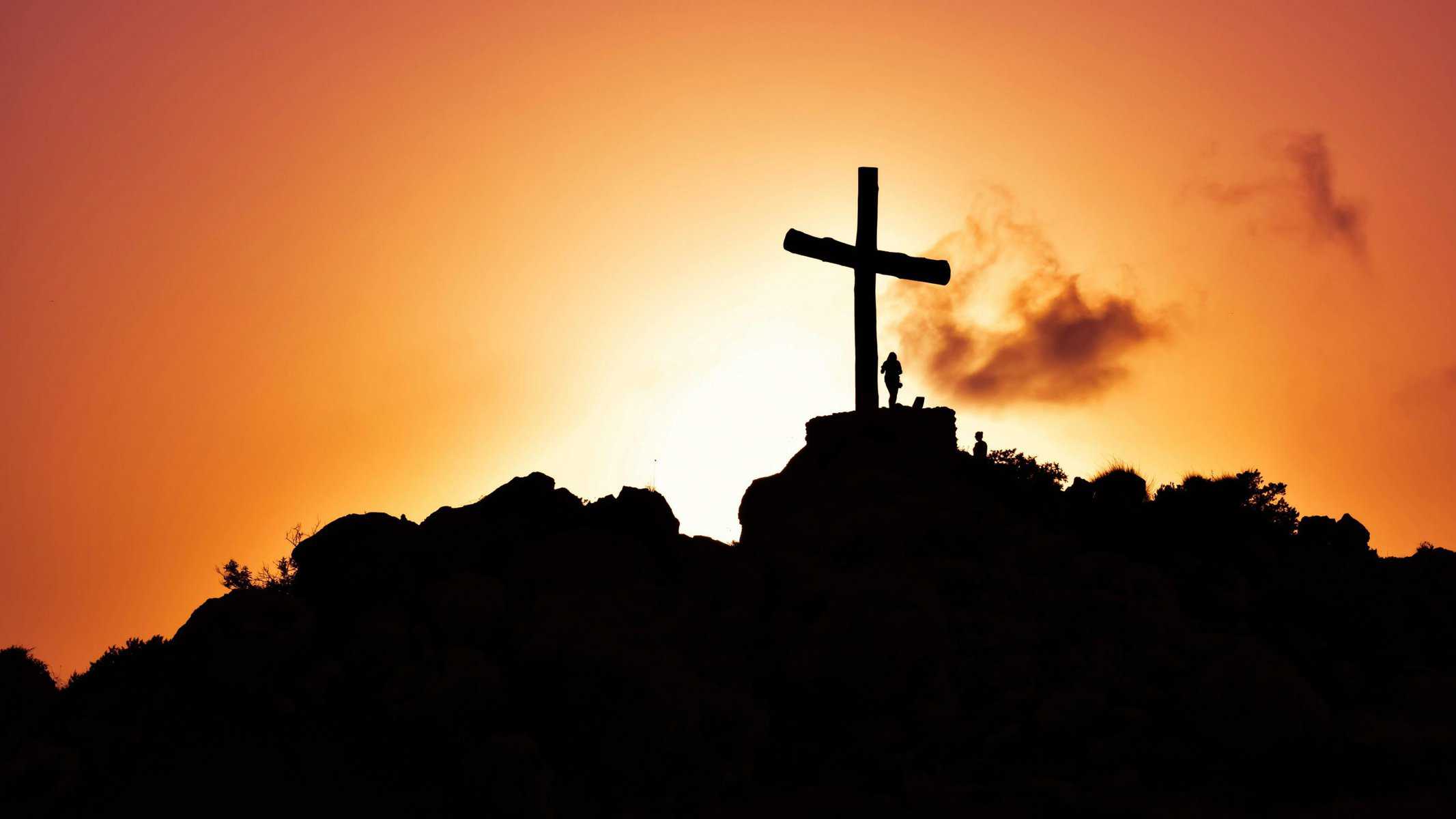 Silhouette of Jesus on the cross during a vibrant sunset sky.