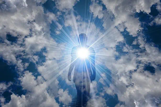 Sunlit silhouette of a person standing against a bright sun and dramatic clouds in the sky.