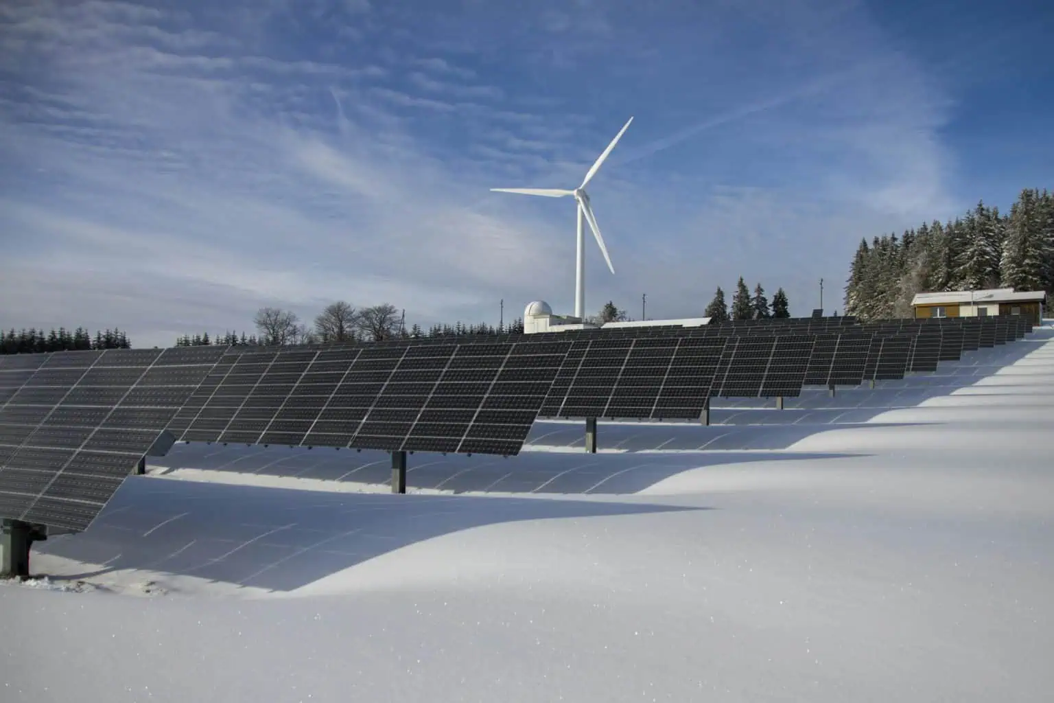 Renewable energy solar panels and wind turbine in snowy landscape.
