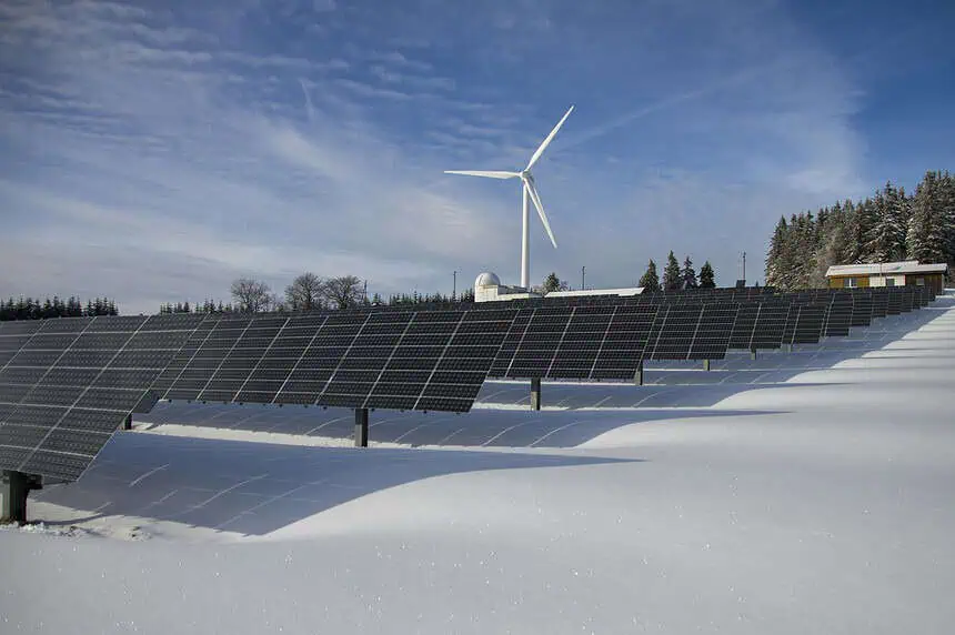 Renewable energy solar panels and wind turbine in snowy landscape.