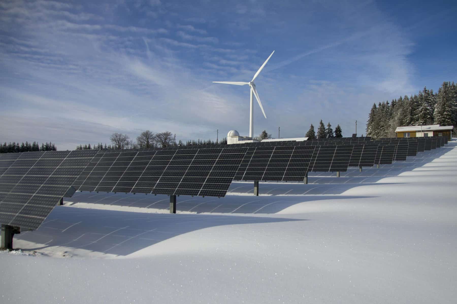Renewable energy solar panels and wind turbine in snowy landscape.