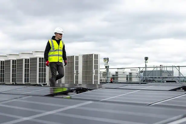 Solar panel technician inspecting rooftop solar panels under cloudy sky.