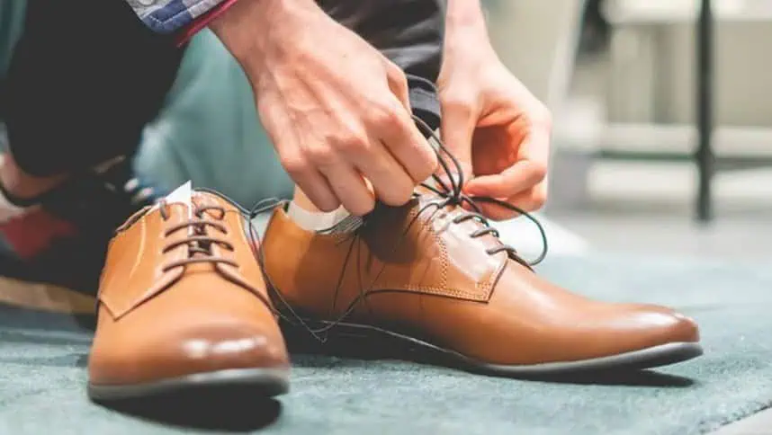 Men tying shoelaces on brown leather dress shoes.