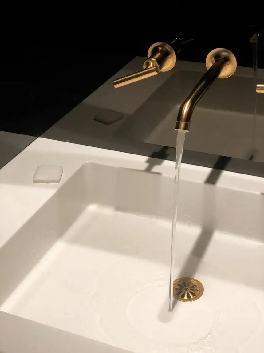 Bathroom sink with flowing water and elegant gold faucet fixtures.