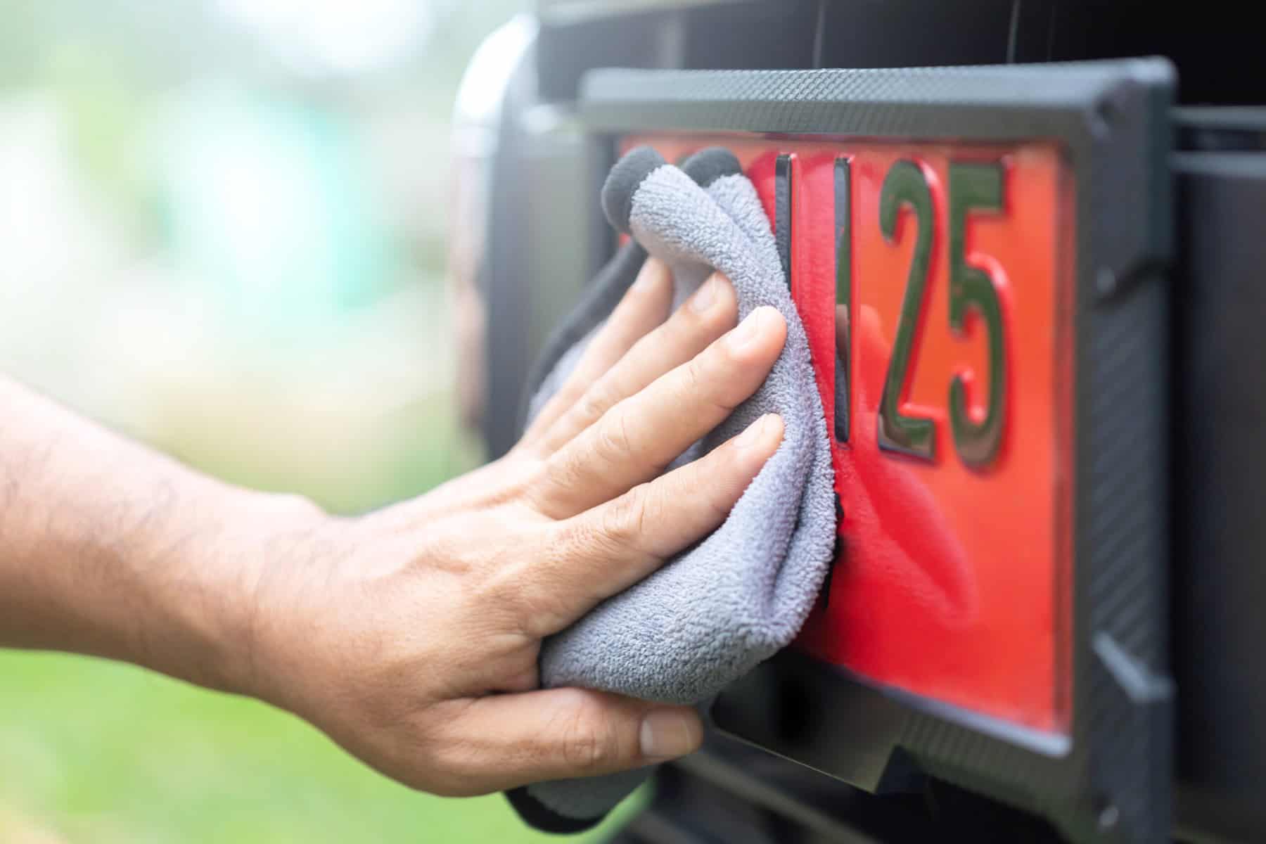 Close-up of hand wiping car license plate with microfiber cloth, outdoors.