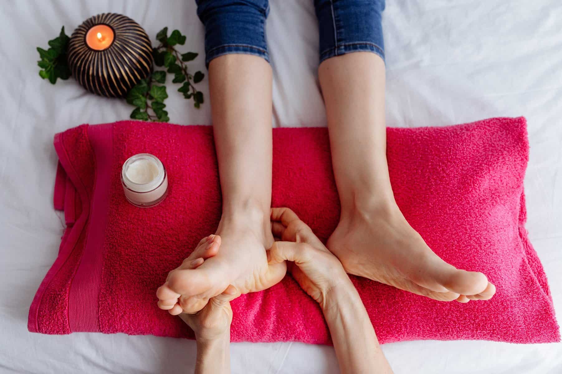 Foot massage therapy in a relaxing spa setting with a pink towel and candles.
