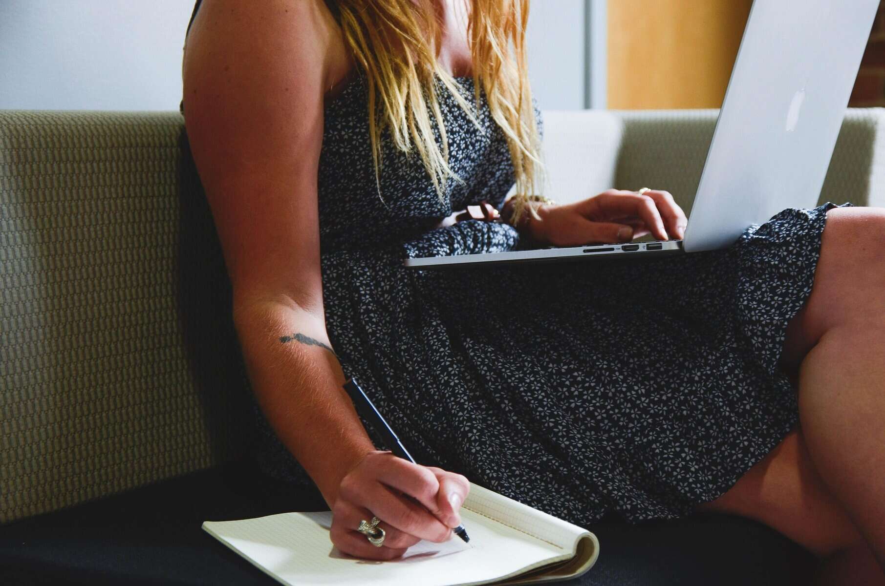 Alt text: Woman working on laptop, taking notes with a pen and notebook nearby.
