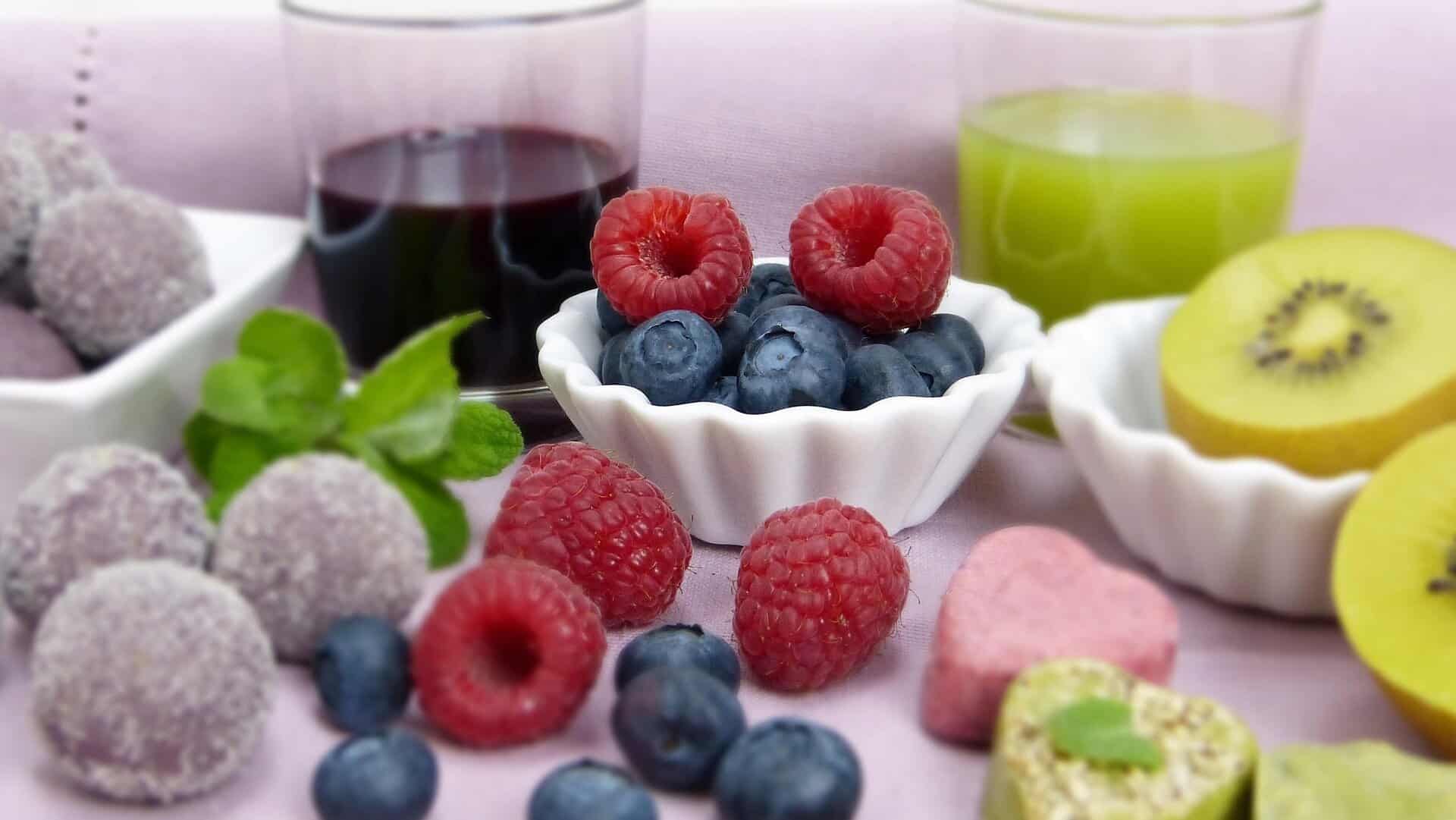 Close-up of fresh blueberries, raspberries, and kiwi slices with drinks in the background.
