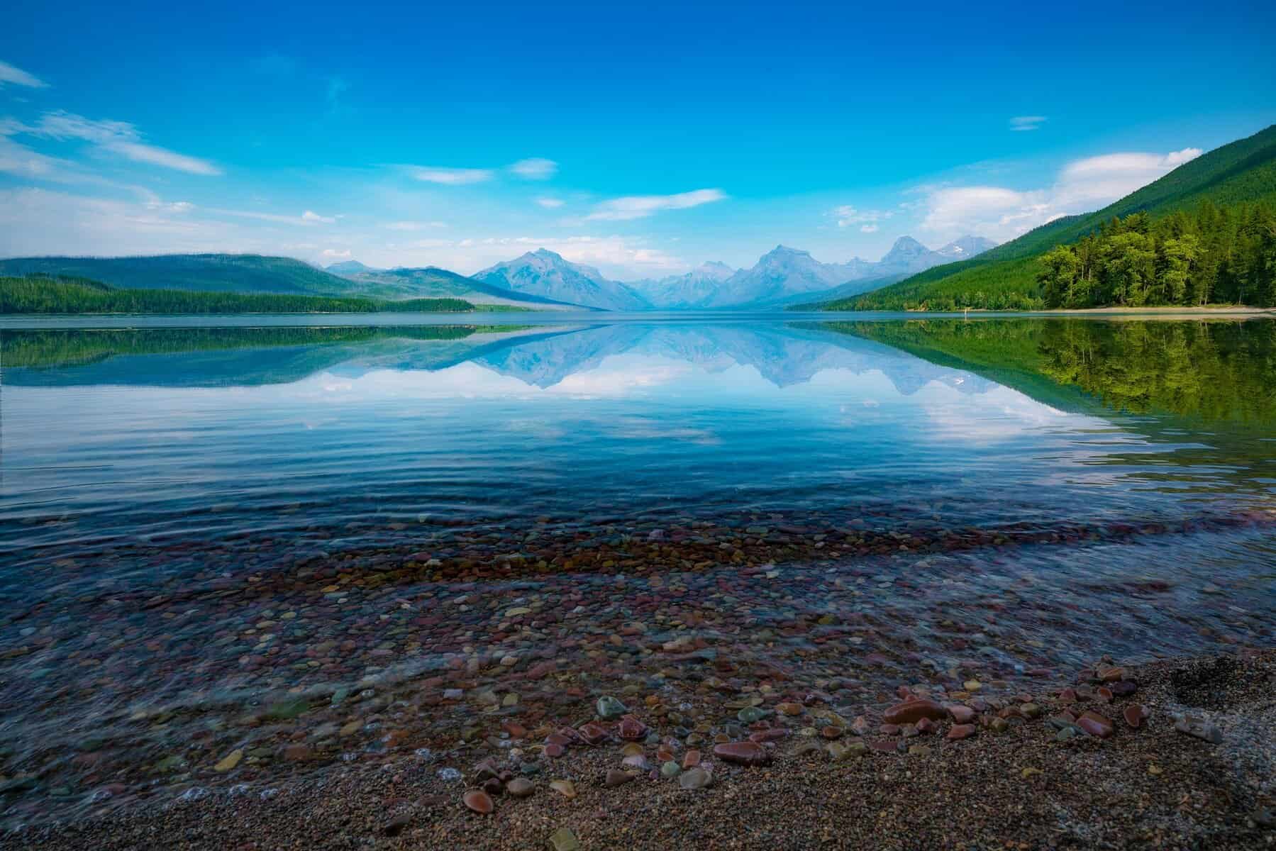 Beautiful mountain lake surrounded by lush greenery and distant snow-covered mountains.
