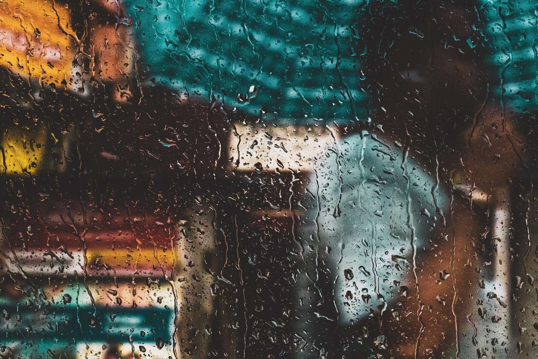 Raindrops on a glass window showcasing a blurred urban city scene with colorful city lights behind.