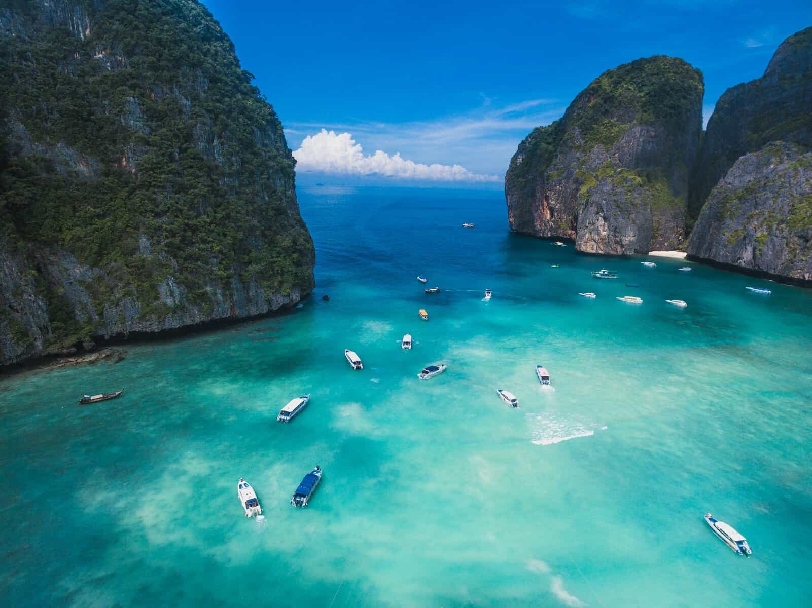 Stunning tropical lagoon with clear blue waters, green cliffs, and boats on the surface.