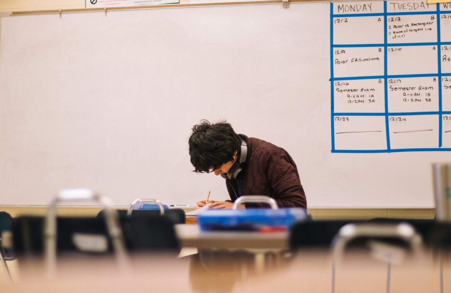 Young student concentrating on homework at school desk with classroom background.