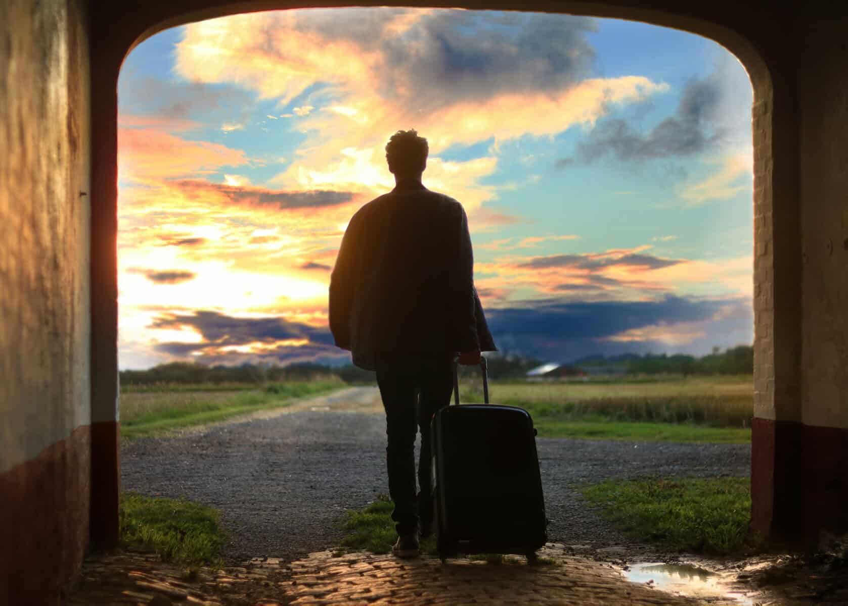 A traveler with a suitcase standing at sunset, gazing at a colorful sky, perfect for travel and adventure inspiration.