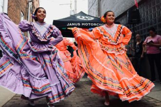 Colorful Mexican folkloric dancers in traditional dresses performing lively dance at outdoor event.