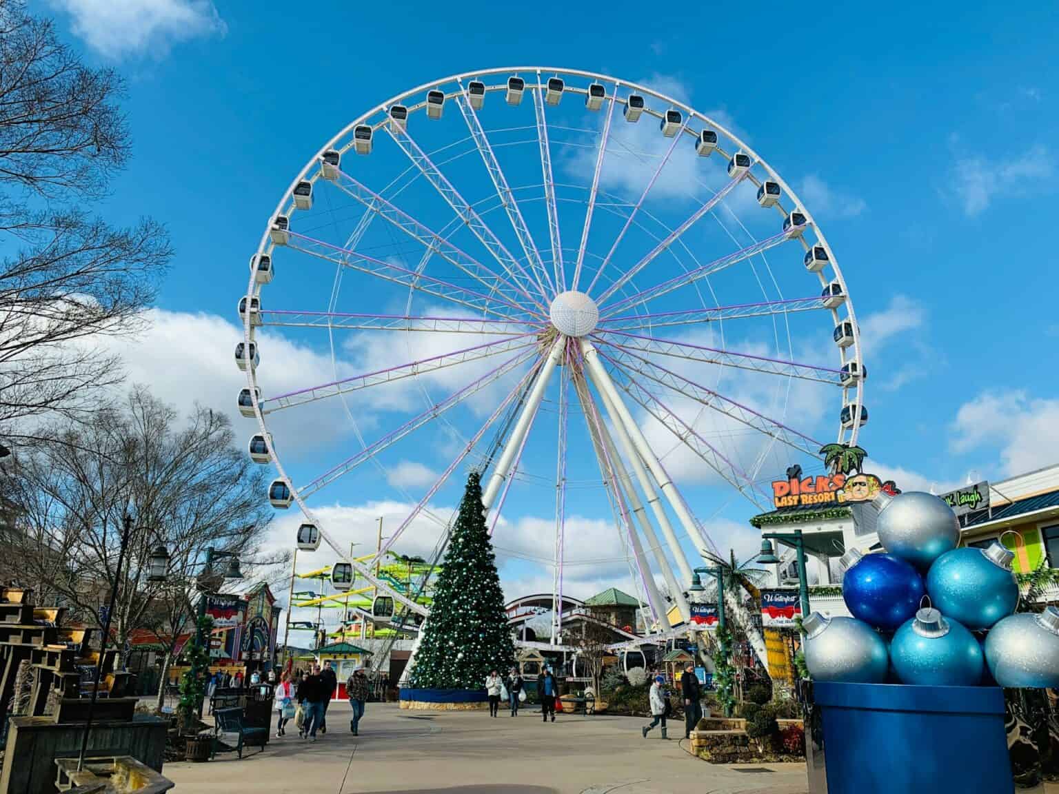 Bright Ferris wheel with gondolas under blue sky, holiday decorations, and visitors enjoying the park.